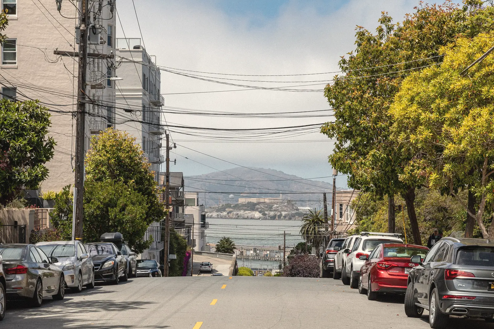 Photo of a residential street with parked cars sloping down toward the bay and Alcatraz